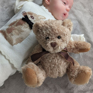 Baby with brown classic teddy bear wearing a bow.