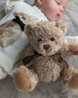 Baby with brown classic teddy bear wearing a bow.