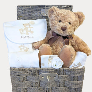 Baby hamper basket packed with gifts. Includes teddy and white baby clothes set.