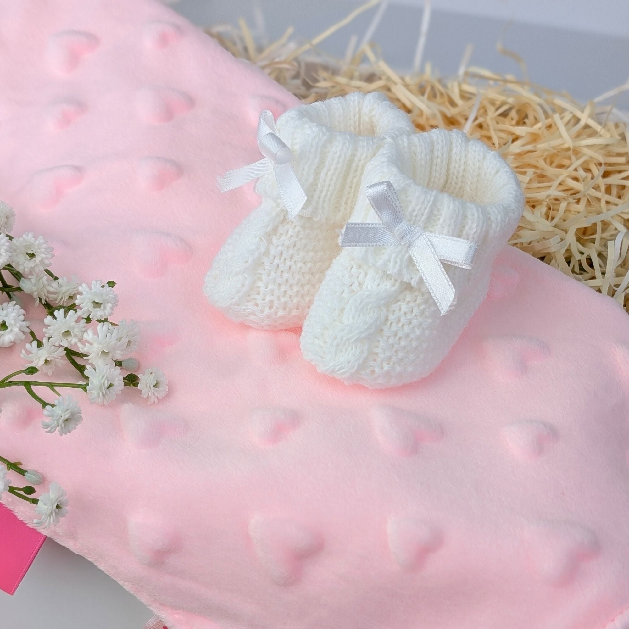 white baby booties on a pink taggie sensory blanket