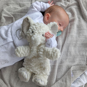 white elephant soft toy cuddled by a baby in white baby clothes set.