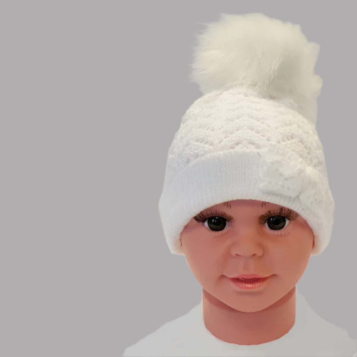 A soft white knitted hat with a bow and pom pom