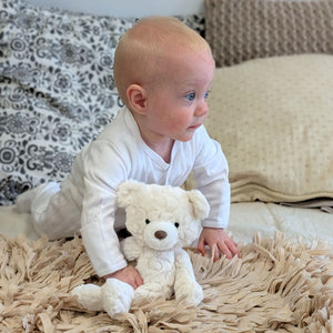 Baby crawling with a white teddy bear.